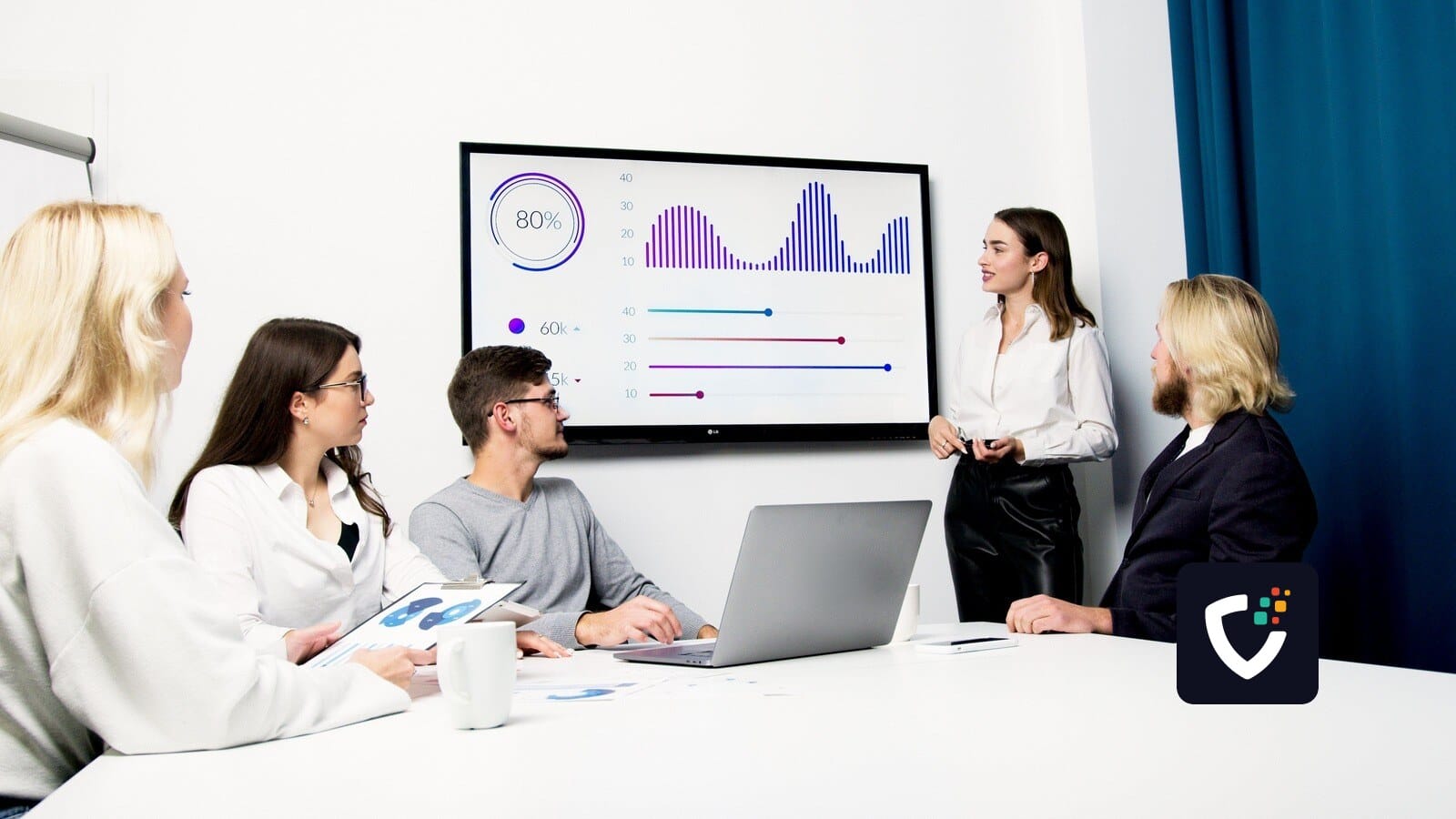 A team in a meeting room looking at charts on a wall-mounted screen