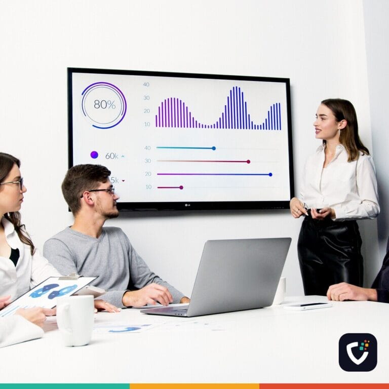 A team in a meeting room looking at charts on a wall-mounted screen