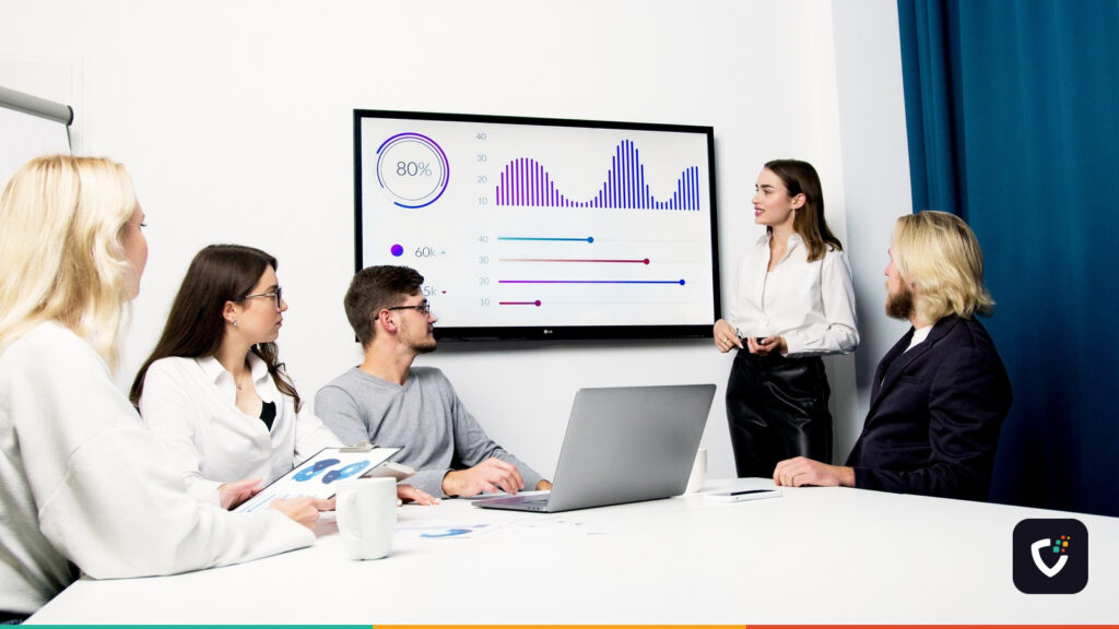 A team in a meeting room looking at charts on a wall-mounted screen