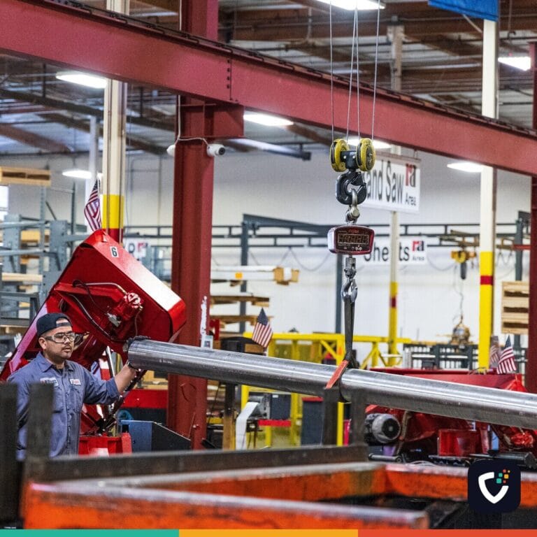 Worker operating heavy machinery in a factory, moving steel bars. Industrial scene indoors