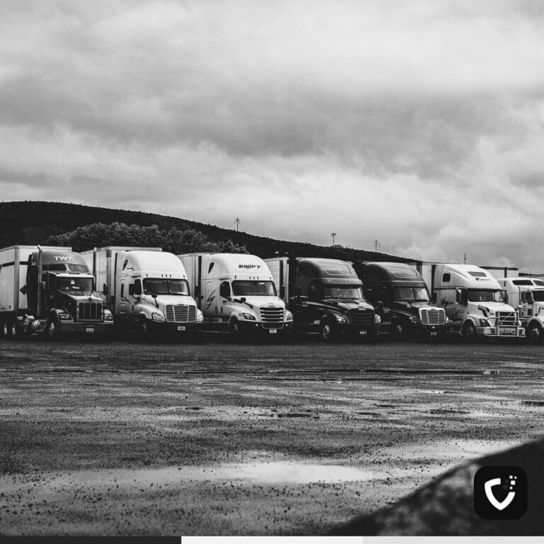 A row of parked American articulated trucks in a wet lot under heavy cloud.