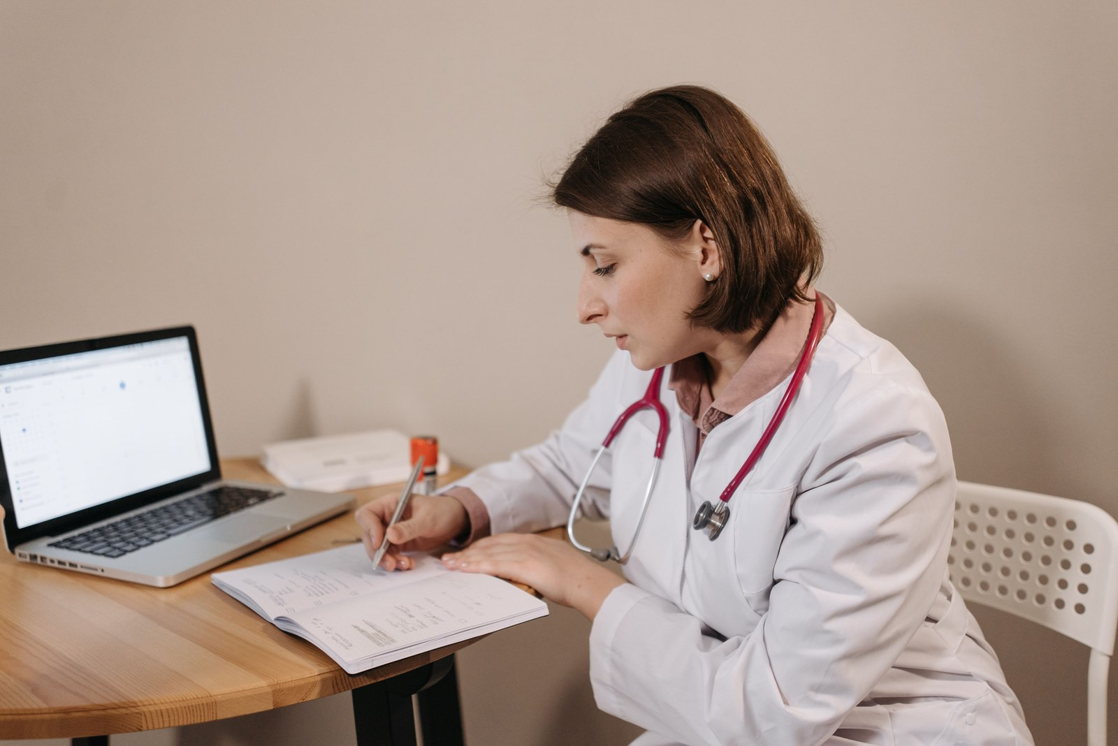 A clinician at an ordinary desk after clinic, seen from behind, with an empty patient chair and paperwork nearby.