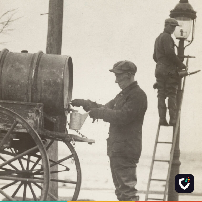 A black and white press photograph from 1926. A lamplighter in a flat cap fills a can from a tank on a horse cart, while a second man stands on a ladder at the top of a gas street lamp, servicing it.