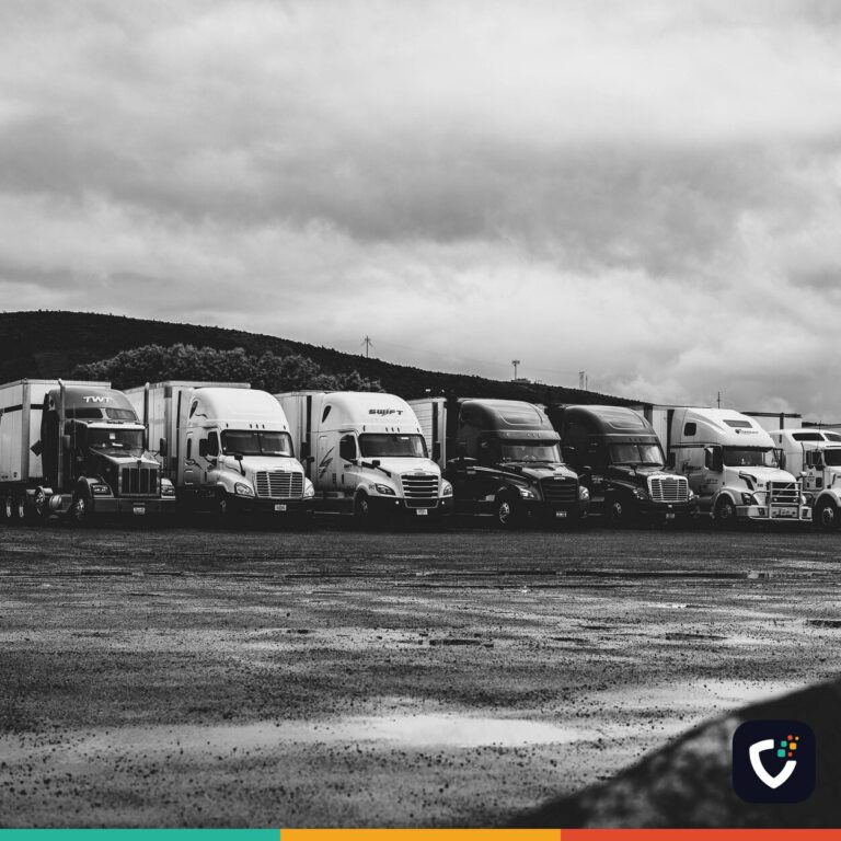 A row of parked American articulated trucks in a wet lot under heavy cloud.