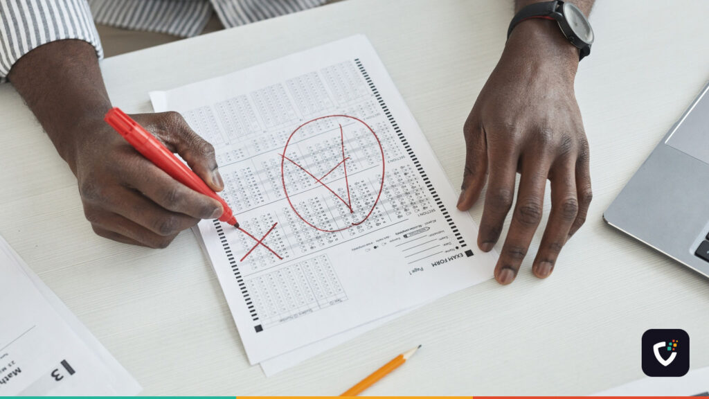 Hands marking a test paper in red pen, a tick circled and crosses beside the answers.